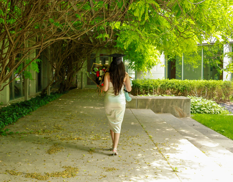 Special occasion photography session in Toronto capturing a woman in a white dress walking outdoors under greenery for a milestone celebration.